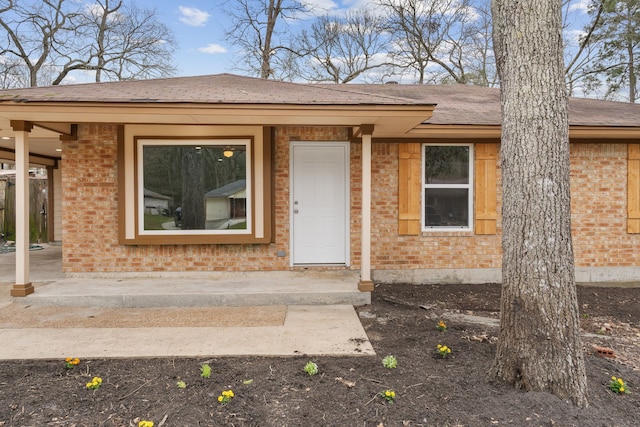 property entrance featuring brick siding and roof with shingles