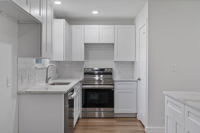 kitchen with light stone countertops, light wood finished floors, a sink, stainless steel appliances, and white cabinetry