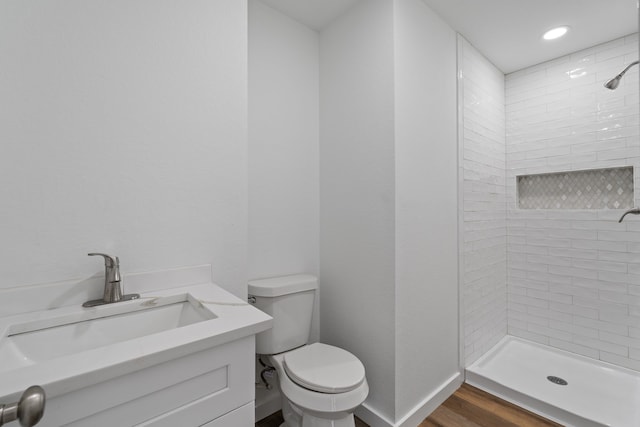 bathroom with vanity, wood finished floors, baseboards, a tile shower, and toilet