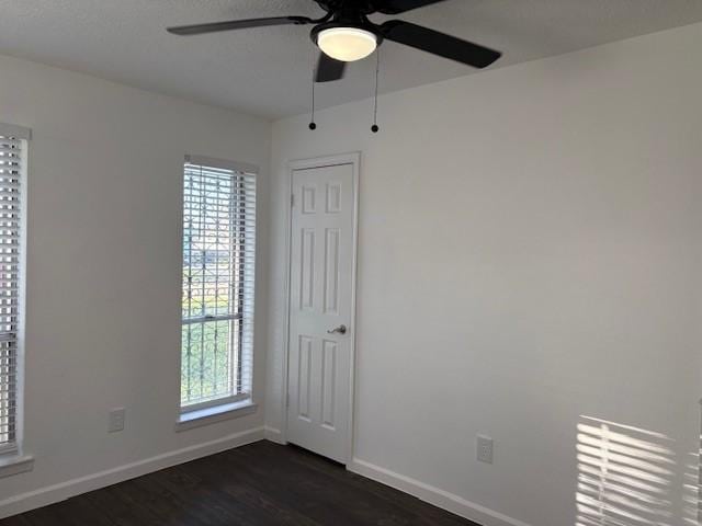 spare room featuring baseboards, dark wood finished floors, and a ceiling fan