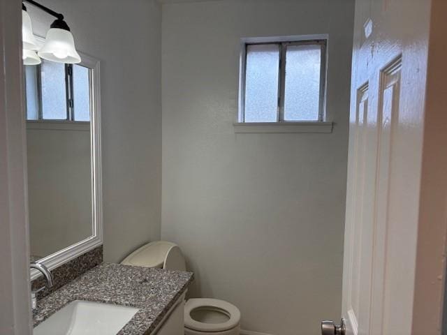 half bathroom with baseboards, toilet, and vanity