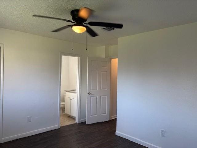 unfurnished bedroom featuring visible vents, baseboards, wood finished floors, a textured ceiling, and ensuite bath