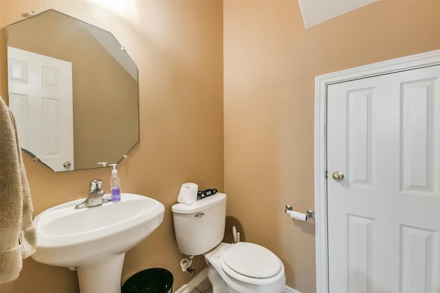 half bathroom featuring toilet, baseboards, and a sink