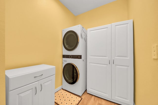 laundry room with cabinet space, stacked washer and dryer, and light wood finished floors