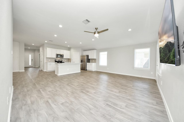 unfurnished living room featuring a ceiling fan, light wood-style flooring, baseboards, and visible vents