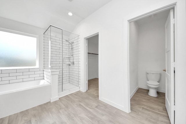 full bath featuring wood finished floors, a shower stall, a walk in closet, a garden tub, and toilet