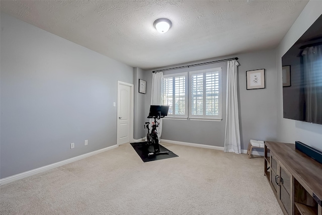 exercise area with baseboards, light colored carpet, and a textured ceiling