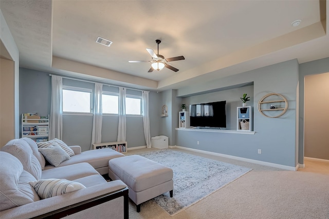 living room with visible vents, baseboards, a tray ceiling, ceiling fan, and light carpet