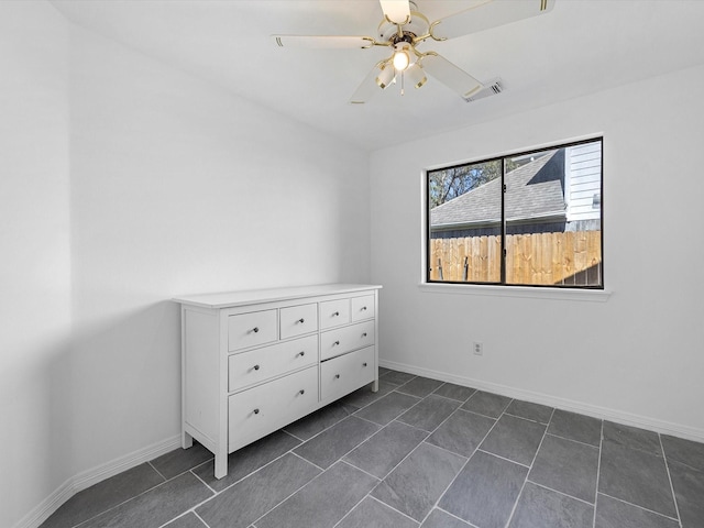 empty room featuring dark tile patterned flooring, a ceiling fan, visible vents, and baseboards