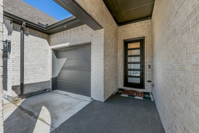 entrance to property with a garage, brick siding, roof with shingles, and driveway