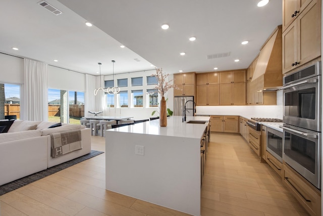 kitchen with visible vents, wall chimney range hood, light countertops, light wood-style flooring, and stainless steel appliances