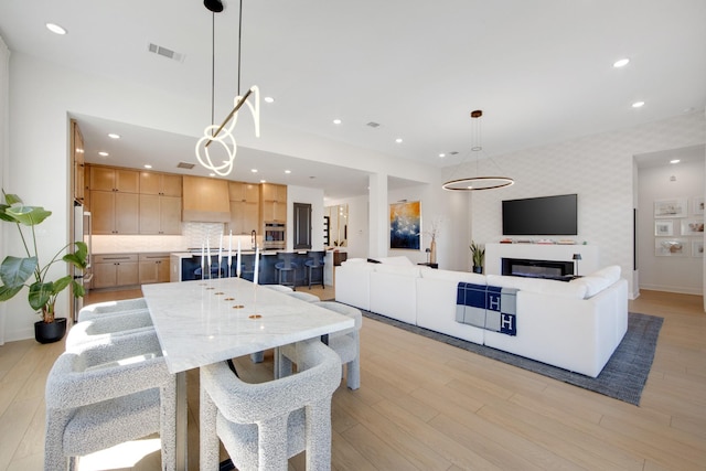 dining room featuring light wood-type flooring, recessed lighting, wallpapered walls, and an accent wall