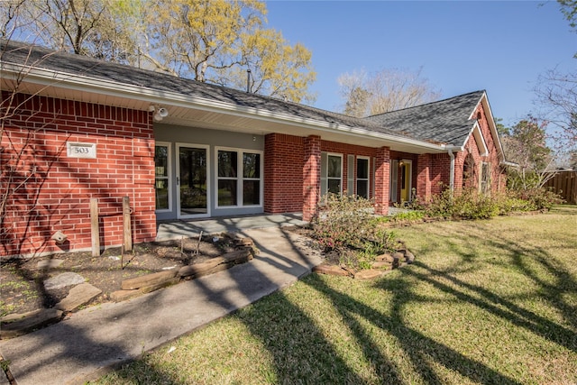 rear view of house with brick siding, a yard, and roof with shingles