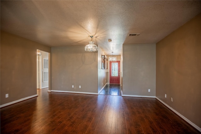 unfurnished room with visible vents, dark wood finished floors, and a chandelier