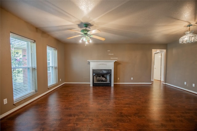 unfurnished living room with a fireplace, baseboards, ceiling fan, and dark wood-style flooring