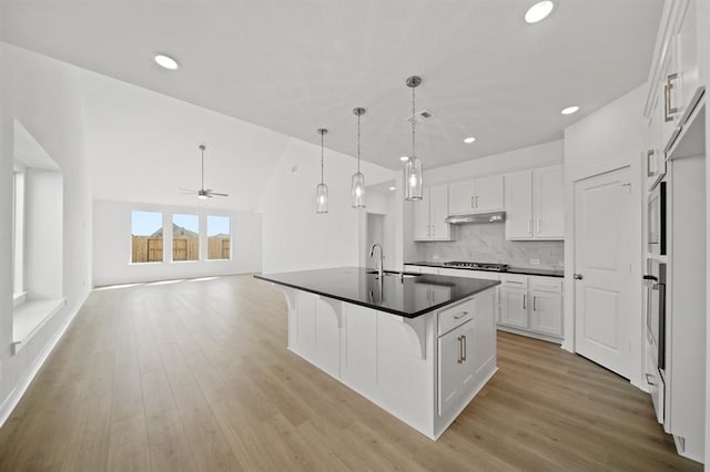 kitchen featuring under cabinet range hood, dark countertops, gas stovetop, light wood-style floors, and white cabinets