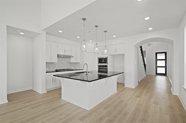 kitchen featuring dark countertops, under cabinet range hood, cooktop, built in microwave, and arched walkways