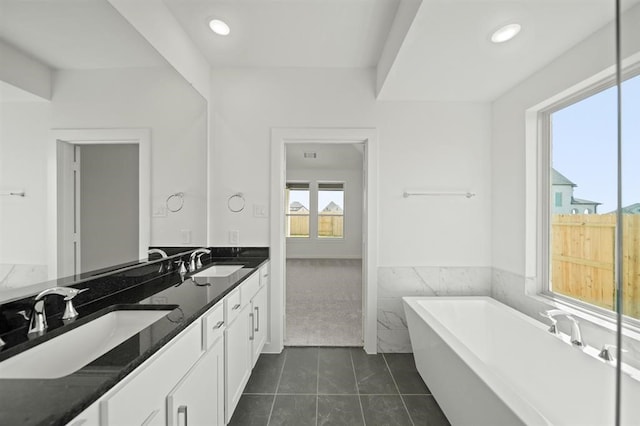 full bath featuring a sink, a freestanding tub, double vanity, and tile patterned floors