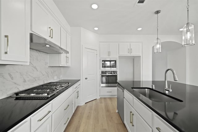 kitchen featuring dark countertops, under cabinet range hood, light wood-style floors, stainless steel appliances, and a sink