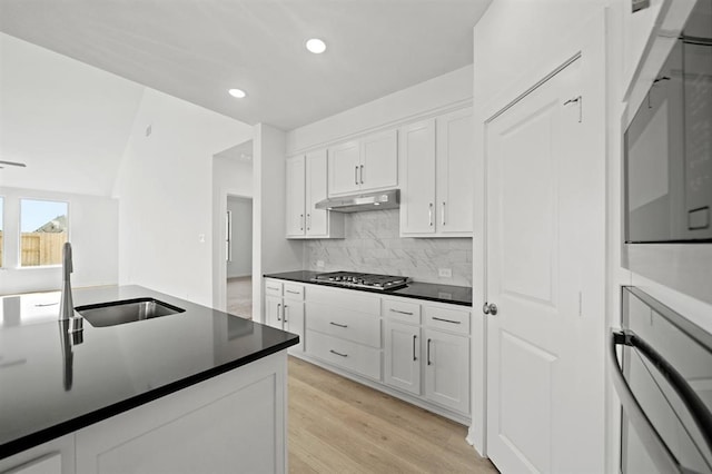 kitchen with a sink, under cabinet range hood, dark countertops, white cabinetry, and stainless steel gas stovetop