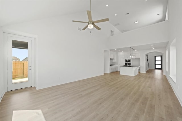 unfurnished living room featuring light wood-type flooring, arched walkways, visible vents, and ceiling fan