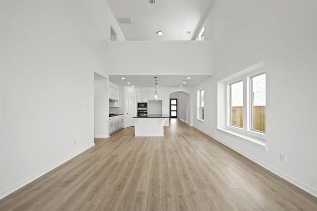 unfurnished living room featuring visible vents, baseboards, recessed lighting, arched walkways, and light wood-type flooring