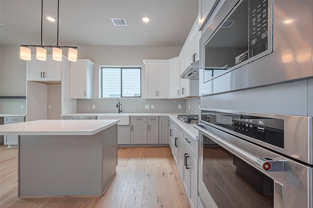 kitchen with tasteful backsplash, under cabinet range hood, light wood-type flooring, light countertops, and appliances with stainless steel finishes