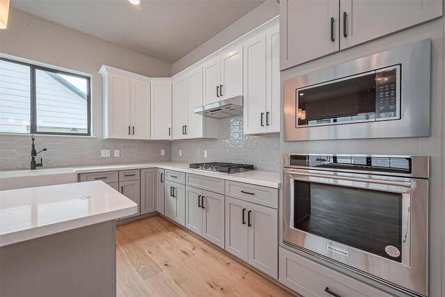 kitchen with under cabinet range hood, light wood finished floors, stainless steel appliances, and light countertops