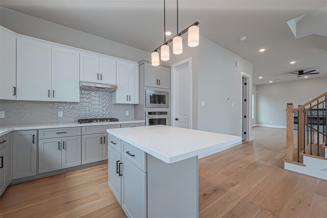 kitchen with backsplash, under cabinet range hood, light wood-type flooring, light countertops, and stainless steel appliances