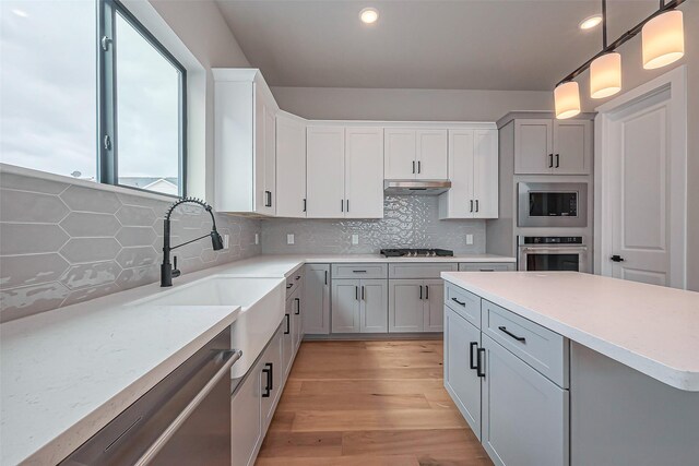 kitchen with under cabinet range hood, stainless steel appliances, decorative backsplash, and light countertops