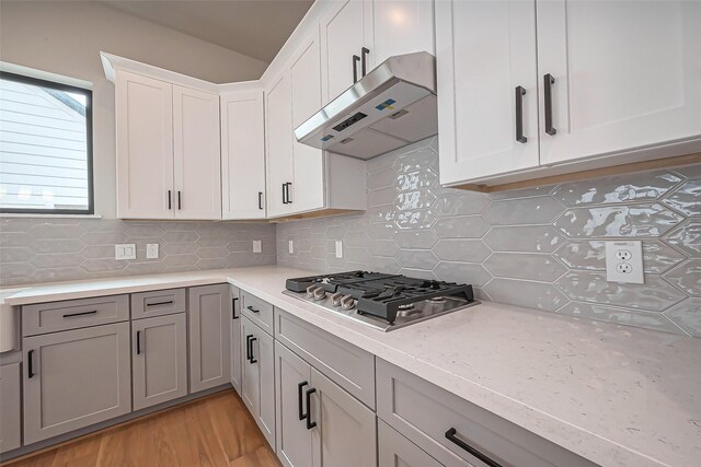 kitchen featuring under cabinet range hood, decorative backsplash, light wood-style flooring, stainless steel gas stovetop, and white cabinets