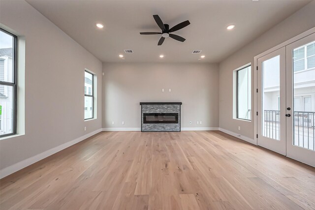 unfurnished living room with light wood-type flooring, french doors, a stone fireplace, and visible vents