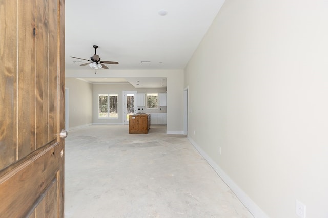 unfurnished living room with unfinished concrete floors, baseboards, and ceiling fan