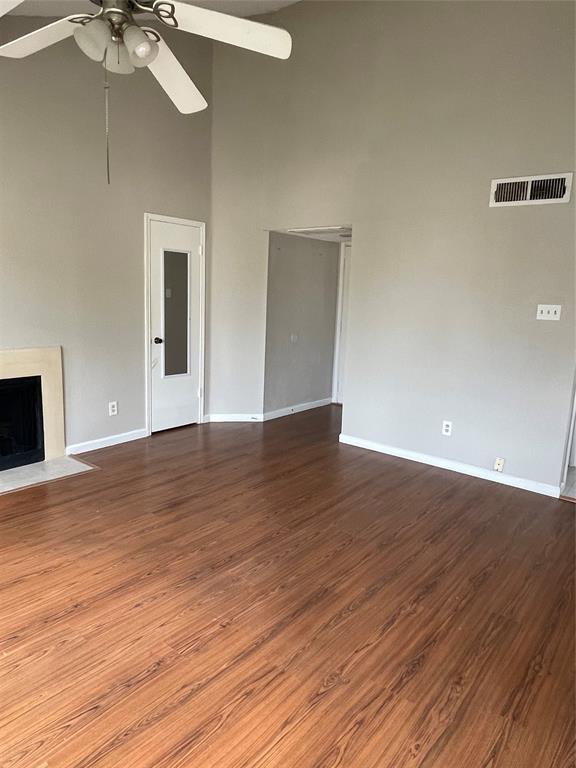 12400 Overbrook Ln Unit 45C, Houston, TX 77077 - unfurnished living room with a towering ceiling, a ceiling fan, dark wood-type flooring, baseboards, and a fireplace with flush hearth