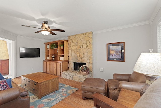 living area featuring a stone fireplace, light wood-style flooring, crown molding, and ceiling fan