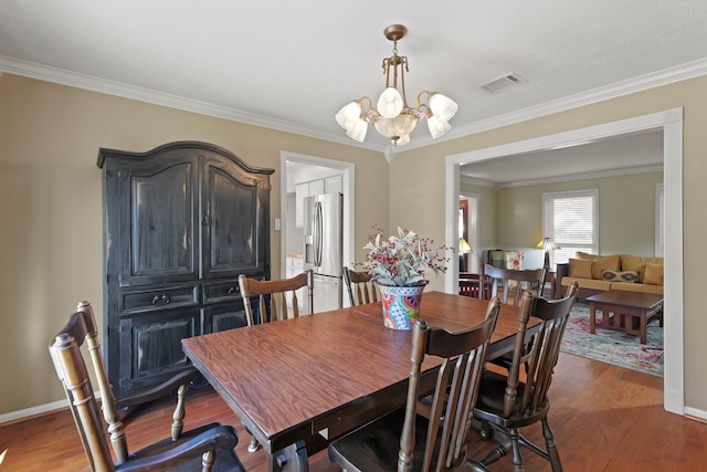 dining area featuring visible vents, an inviting chandelier, wood finished floors, and crown molding