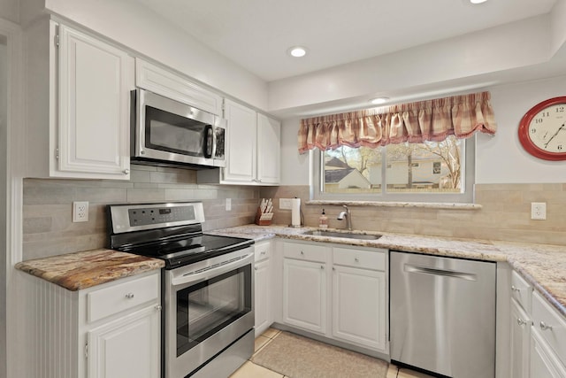 kitchen featuring a sink, light stone counters, appliances with stainless steel finishes, white cabinets, and decorative backsplash