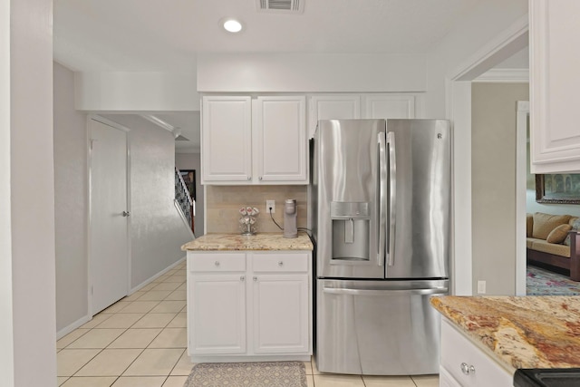 kitchen with light stone counters, light tile patterned floors, visible vents, stainless steel refrigerator with ice dispenser, and white cabinetry