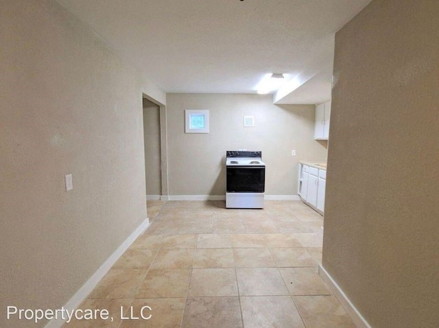 kitchen featuring baseboards, light countertops, light tile patterned floors, white cabinetry, and white electric range