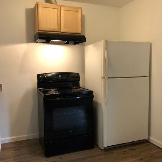 kitchen with light brown cabinets, black electric range oven, under cabinet range hood, freestanding refrigerator, and dark wood-style flooring