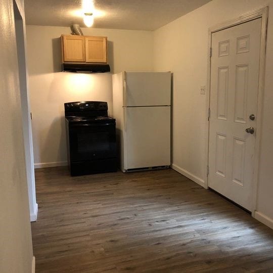 kitchen with under cabinet range hood, dark wood-style floors, black range with electric cooktop, and freestanding refrigerator