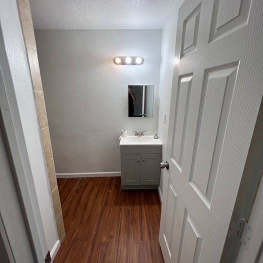 bathroom with a textured ceiling, vanity, baseboards, and wood finished floors