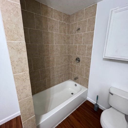 full bath featuring toilet, shower / bathtub combination, baseboards, and wood finished floors