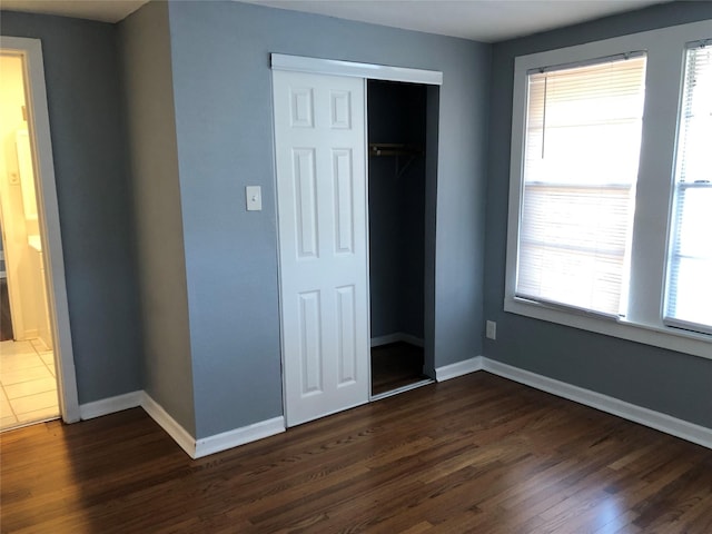 unfurnished bedroom featuring baseboards, multiple windows, a closet, and dark wood finished floors