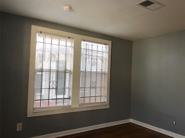 unfurnished room featuring visible vents, baseboards, dark wood-type flooring, and a healthy amount of sunlight