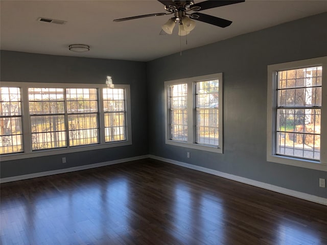 unfurnished room featuring dark wood-style flooring, visible vents, and a wealth of natural light