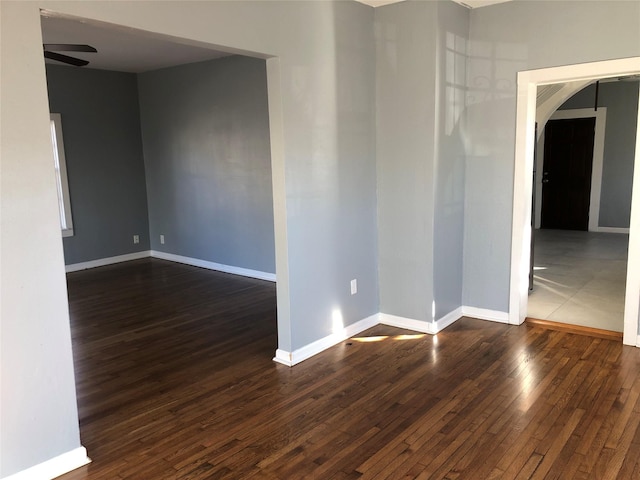 empty room with arched walkways, dark wood finished floors, a ceiling fan, and baseboards