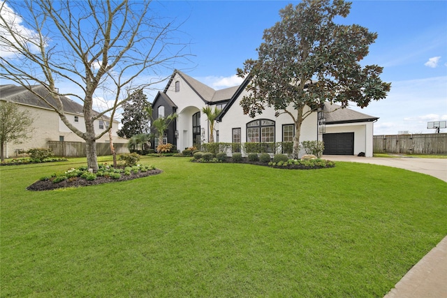 french provincial home with an attached garage, concrete driveway, a front lawn, and fence