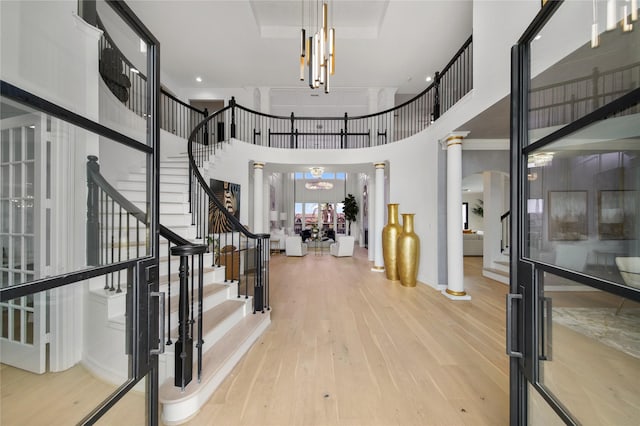 entrance foyer featuring a notable chandelier, light wood-style floors, stairs, and ornate columns