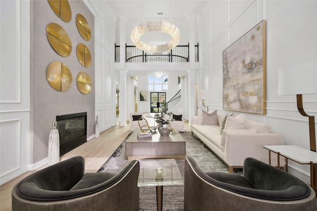 living area with wood finished floors, decorative columns, stairs, a glass covered fireplace, and a decorative wall